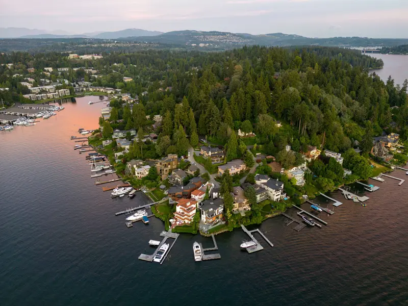 A wooded shoreline point with houses and docks seen from above at sunset, the lake around it.