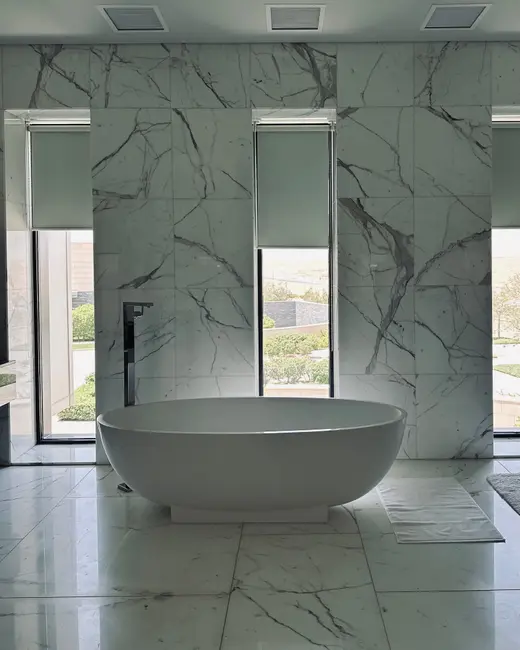 A freestanding tub in a marble bathroom with a window at the end.