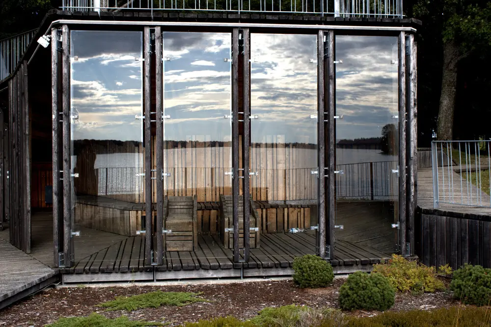Floor-to-ceiling glass panels on a lakeside house reflecting a cloudy evening sky and the water.