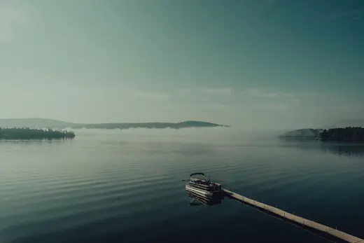 A small boat tied at the end of a dock on a still, misty lake at first light.
