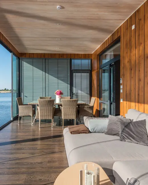 A wood-panelled room with a pale sofa and a dining table beside glass doors onto the water.